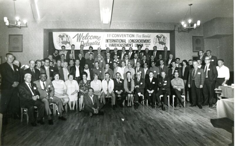 Group photograph of ILWU convention delegates in a union hall beneath a Welcome Delegates banner